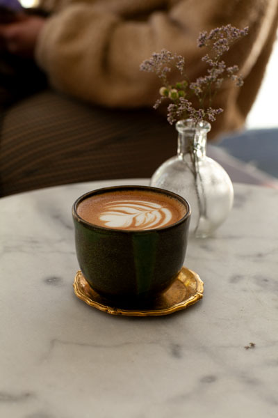 Eine grüne Tasse mit Milchkaffe steht auf einem Marmortisch mit Vase.